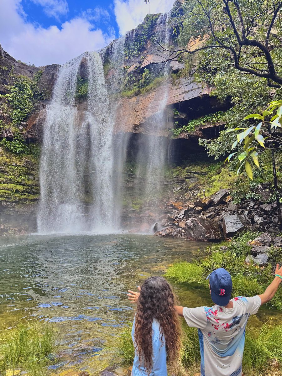 Casal apontando para uma cachoeira alta ao fim da trilha